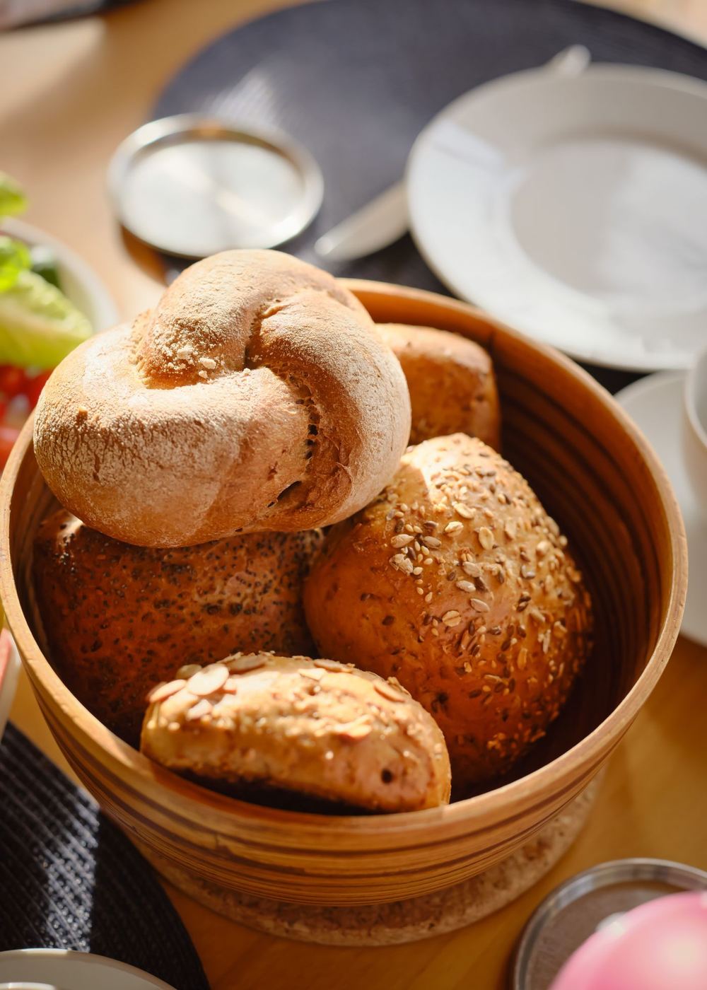A wooden bowl of crusty bread rolls
